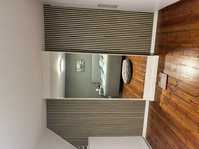 Afgewerkte kamer met houten lattenwand rond een spiegelkast en een parketvloer